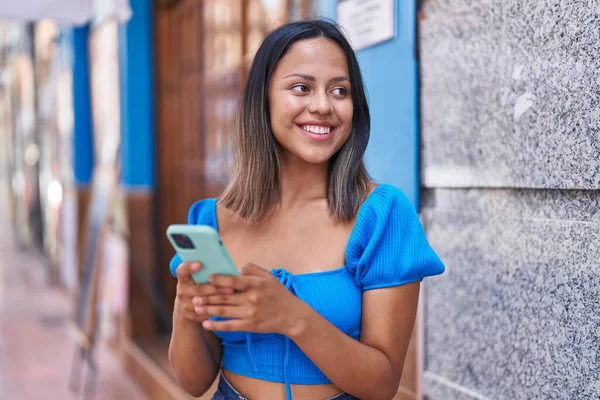 若いヒスパニック系の女性が自信を持って笑顔でスマートフォンを使って通り — ストック写真
