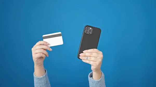 年轻的惊慌失措的女人带着智能手机和信用卡在网上做着离群索居的蓝色背景 — 图库照片