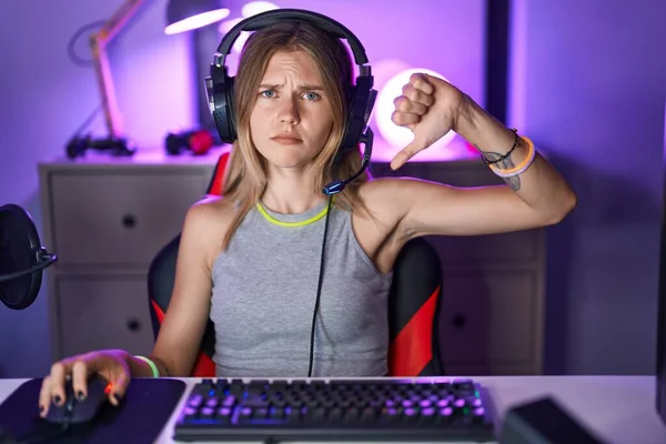ブロンド原因アジアの女性は怒っている顔でヘッドフォンでビデオゲームをプレイします 親指ダウンで嫌いを示す負の記号 拒絶概念 — ストック写真