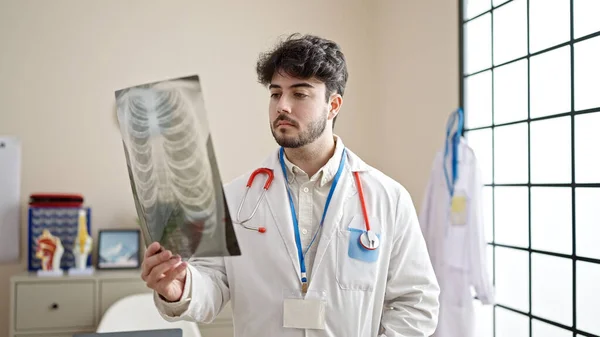 年轻的惊慌失措的男医生带着怀疑的表情看着诊所的X光 — 图库照片