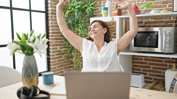 stock image Middle age hispanic woman using laptop stretching arms at dinning room