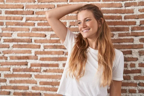 stock image Young caucasian woman standing over bricks wall smiling confident touching hair with hand up gesture, posing attractive and fashionable 