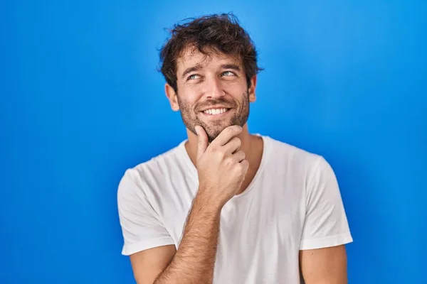 ヒスパニック系の若い男の質問については 集中的な表現を考えて顎の手で青の背景に立っている 笑顔で思いやりのある顔 疑わしい概念 — ストック写真