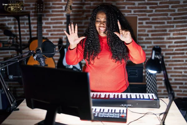 stock image Plus size hispanic woman playing piano at music studio showing and pointing up with fingers number seven while smiling confident and happy. 