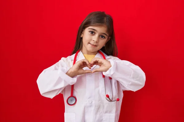 医師の制服を着た小さなヒスパニック系の女の子と手で心のシンボル形状を行う愛に笑みを浮かべて聴診器 ロマンチックなコンセプト — ストック写真