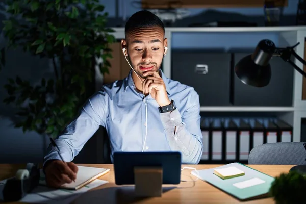 stock image Young hispanic man working at the office at night thinking worried about a question, concerned and nervous with hand on chin 