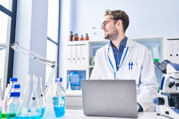 Young man scientist smiling confident using laptop at laboratory
