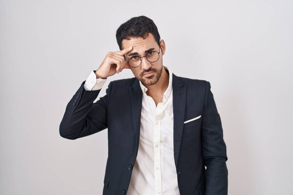 Handsome business hispanic man standing over white background pointing unhappy to pimple on forehead, ugly infection of blackhead. acne and skin problem 