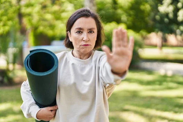 中年时 惊慌失措的女人在公园拿着瑜伽垫 张开手 用严肃而自信的表情和防守的手势做了个停车手势 — 图库照片