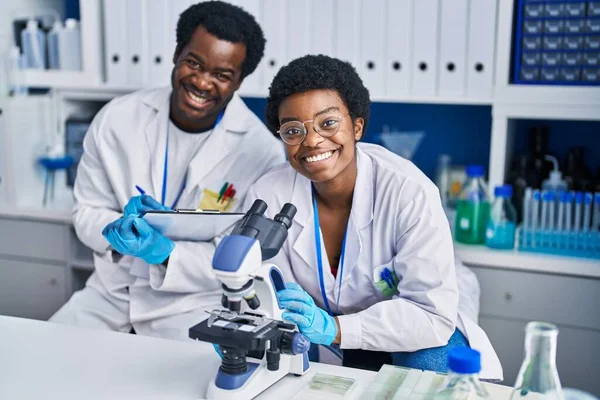 アフリカ系アメリカ人の男性と女性の科学者は 実験室で文書に顕微鏡を使って — ストック写真