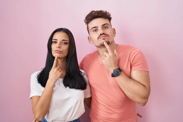 Young Hispanic Couple Standing Pink Background Thinking Concentrated Doubt Finger — Stockfoto