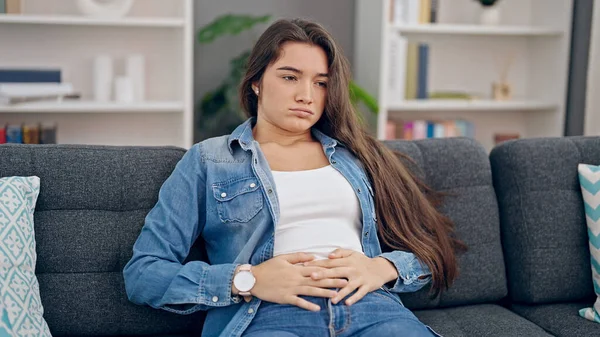 年轻美丽的惊慌失措的女人坐在家里的沙发上肚子疼 — 图库照片