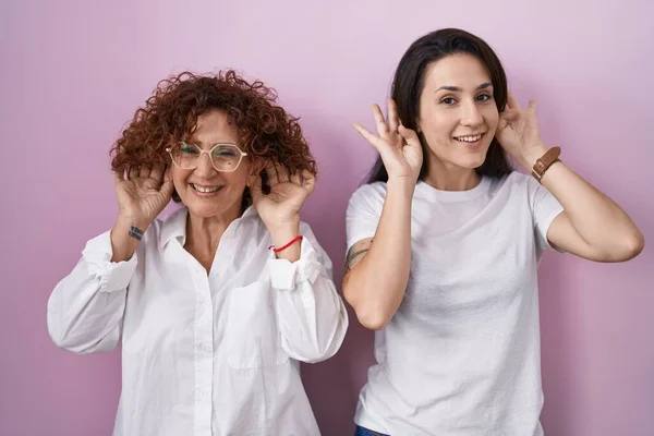 Hispanic Mother Daughter Wearing Casual White Shirt Pink Background Trying — Stockfoto