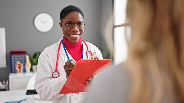 アフリカ系アメリカ人女性医師が診療所で患者と話す医療報告書を書く — ストック写真