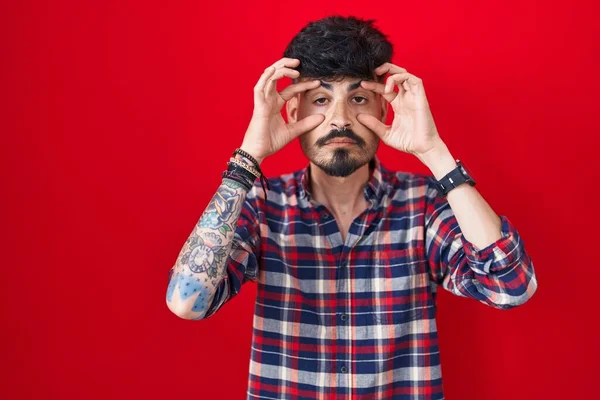 Kırmızı Arka Planda Sakallı Genç Spanyol Bir Adam Gözlerini Parmaklarıyla — Stok fotoğraf