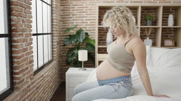 若いです妊娠中の女性タッチ腹座っています上のベッドルーム — ストック写真