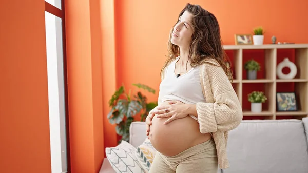 Молодая Беременная Женщина Массирует Живот Стоя Дома — стоковое фото