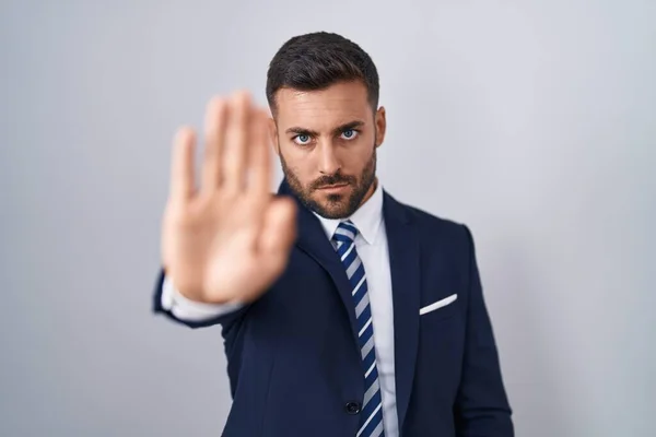 Handsome hispanic man wearing suit and tie doing stop sing with palm of the hand. warning expression with negative and serious gesture on the face.