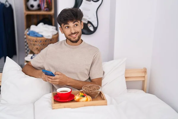 Ung Arabisk Man Med Smartphone Som Äter Frukost Sovrummet — Stockfoto