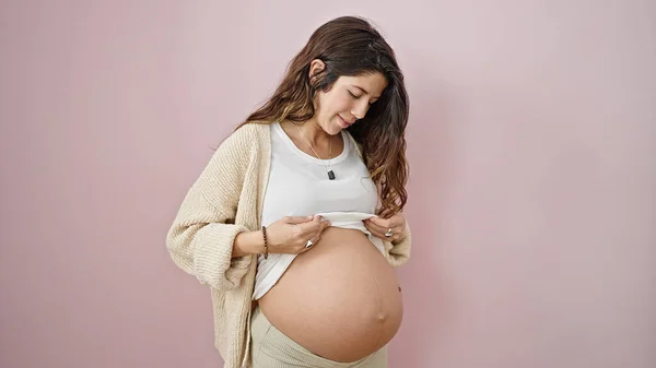 Mladá Těhotná Žena Usmívající Sebevědomě Ukazující Břicho Přes Izolované Růžové — Stock fotografie
