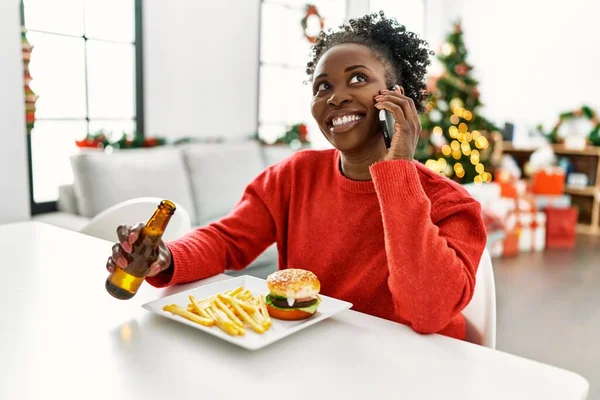 African American Woman Eating Hamburger Talking Smartphone Sitting Table Christmas — Stockfoto