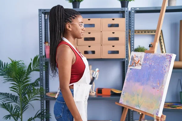 年轻的非洲裔美国人 在画布上的画室画辫子向侧面看 带着自信的微笑放松自己的姿态 — 图库照片