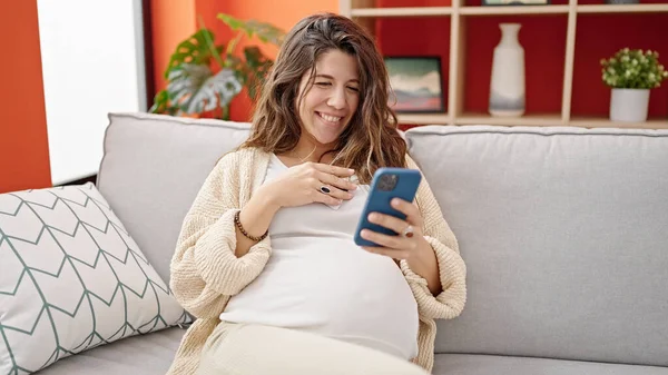 Młoda Kobieta Ciąży Pomocą Smartfona Dotykając Brzucha Domu — Zdjęcie stockowe