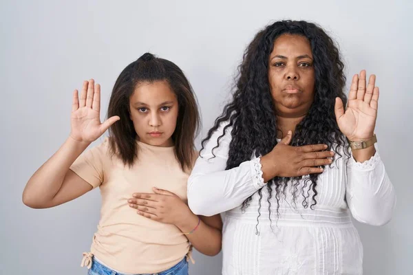 母亲和年幼的女儿站在白种人的背景上 双手托着胸膛 张开手掌 宣誓效忠 — 图库照片