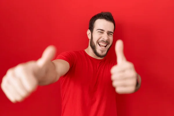 手で積極的なジェスチャーを行うことを承認カジュアルな赤いTシャツを着て若いヒスパニック系の男 親指アップ笑顔と成功のために幸せ 勝者のジェスチャー — ストック写真