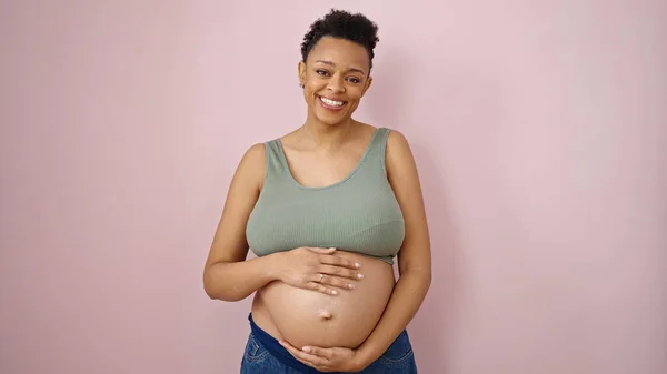 Jonge Zwangere Vrouw Glimlachen Zelfverzekerd Aanraken Buik Geïsoleerde Roze Achtergrond — Stockfoto