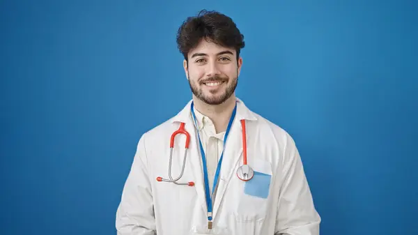 Молодий Іспаномовний Лікар Посміхається Впевнено Стоїть Над Ізольованим Синім Тлом — стокове фото