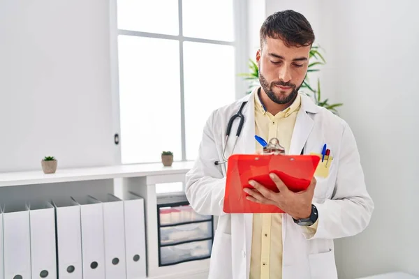 Young Hispanic Man Wearing Doctor Uniform Writing Clipboard Clinic — Zdjęcie stockowe