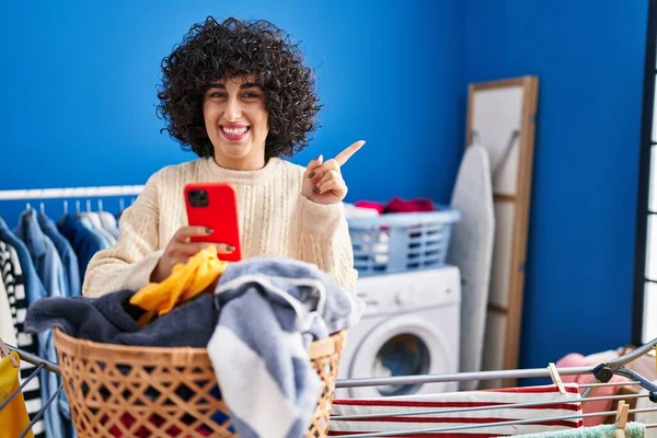 Jovem Morena Com Cabelo Encaracolado Lavando Roupas Usando Smartphone Sorrindo — Fotografia de Stock