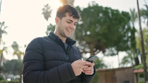 公園で笑顔のスマートフォンを使っている若いヒスパニック系の男 — ストック写真