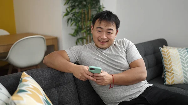 Young Chinese Man Using Smartphone Sitting Sofa Home — Stock fotografie