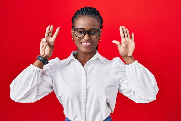 Afrikanerin Mit Zöpfen Steht Auf Rotem Hintergrund Und Zeigt Mit — Stockfoto