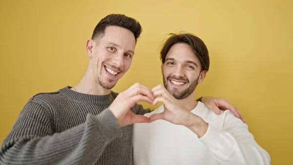 Δύο Άνδρες Ζευγάρι Αγκαλιάζονται Κάνοντας Χειρονομία Καρδιάς Απομονωμένο Κίτρινο Φόντο — Φωτογραφία Αρχείου