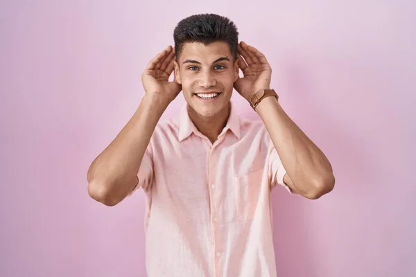 Joven Hombre Hispano Pie Sobre Fondo Rosa Tratando Escuchar Ambas — Foto de Stock