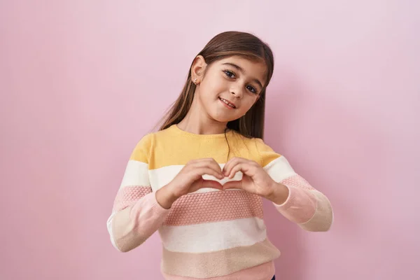 분홍색 배경에 스웨터를 모양을 손으로 좋아하며 스페인 소녀가 낭만적 — 스톡 사진
