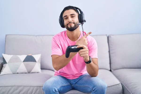 ヒスパニック系の若いです男再生ビデオゲーム保持コントローラー座っています上のソファポインティングに手指で側に示す広告 深刻かつ穏やかな顔 — ストック写真