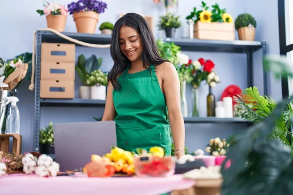 Young hispanic woman florist smiling confident using laptop at florist shop