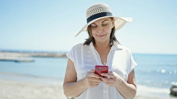 Латиноамериканка Средних Лет Улыбается Используя Смартфон Пляже — стоковое фото