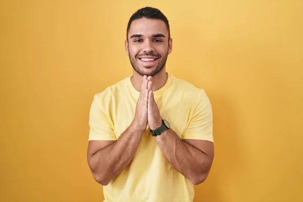 Jovem Hispânico Homem Sobre Fundo Amarelo Orando Com Mãos Juntas — Fotografia de Stock