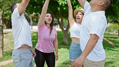 Bir grup insan parkta birlik jesti yaparken kendinden emin gülümsüyor.