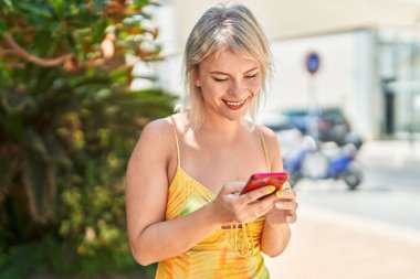 Parkta akıllı telefon kullanan, kendine güvenen genç sarışın kadın.