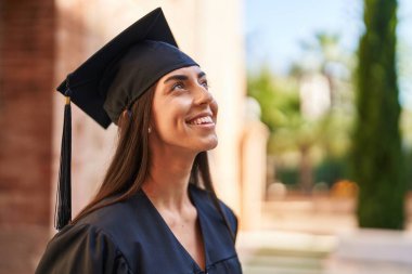 Young hispanic woman wearing graduated uniform looking to the sky at university clipart