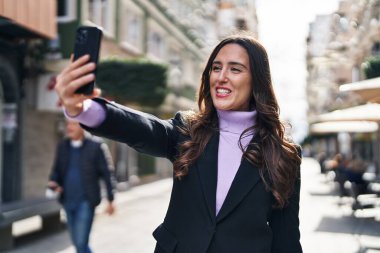 Young hispanic woman smiling confident make selfie by the smartphone at street