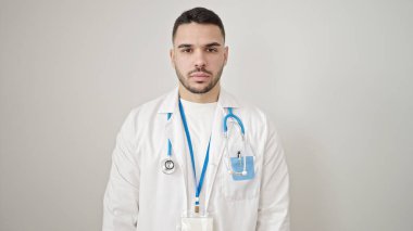 Soyutlanmış beyaz arka planda ciddi bir ifadeyle duran genç İspanyol doktor.