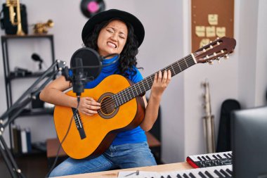 Genç Çinli kadın sanatçı müzik stüdyosunda gitar çalarak şarkı söylüyor.