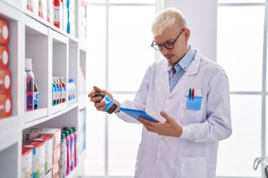 Young caucasian man pharmacist using touchpad holding medicine bottle at pharmacy